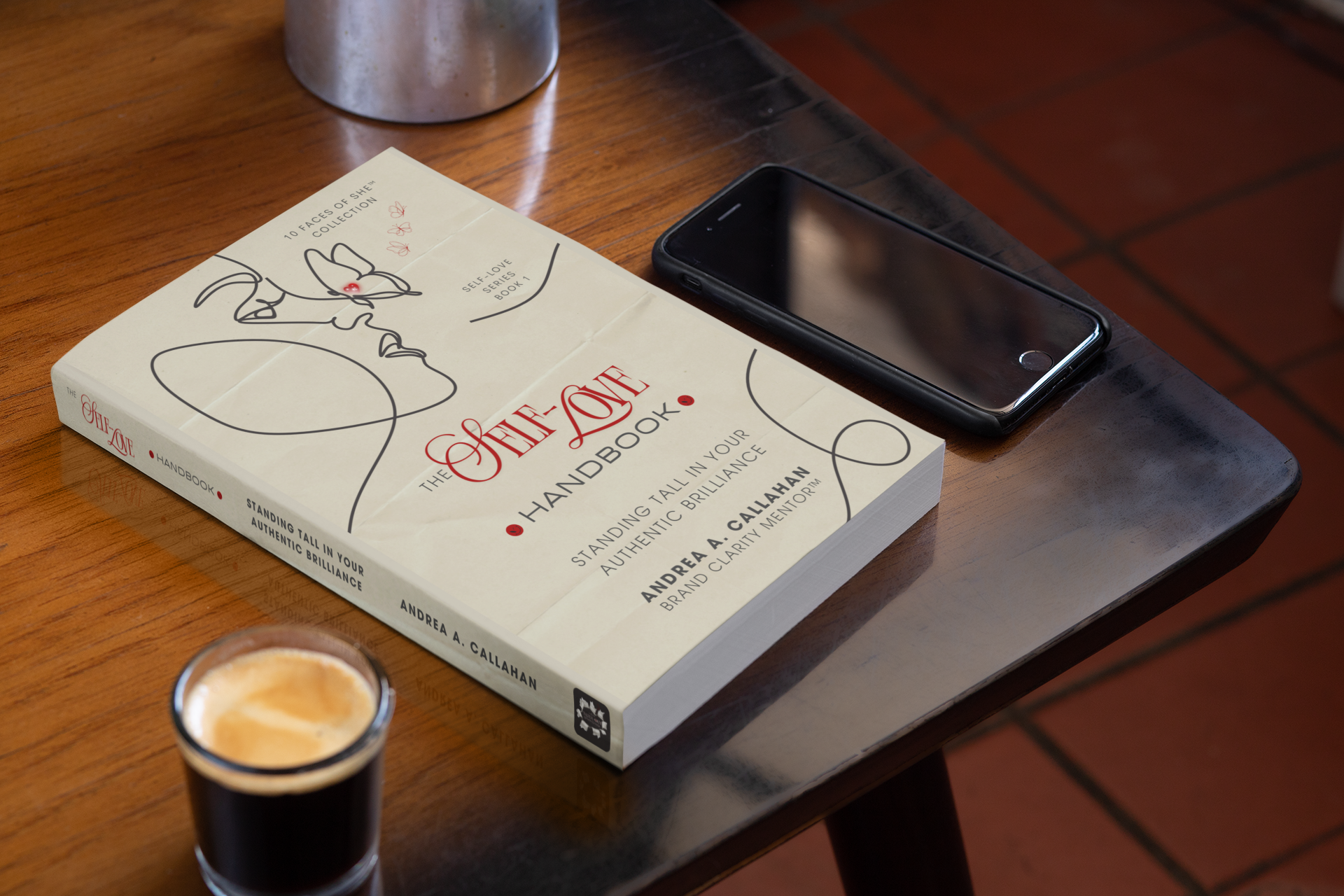 The Self-Love Handbook Stand Tall in Your Authentic Brilliance book by Andrea Callahan on a. table with latte and cell phone
